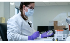 Scientist in white lab coat plates out bacteria onto culture media